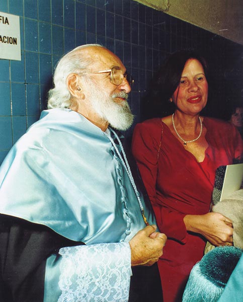 Paulo Freire, de barba blanca y gafas, con la toga azul claro de doctor honoris causa, junto a una mujer con vestido rojo y collar de perlas. Madrid, 1991.