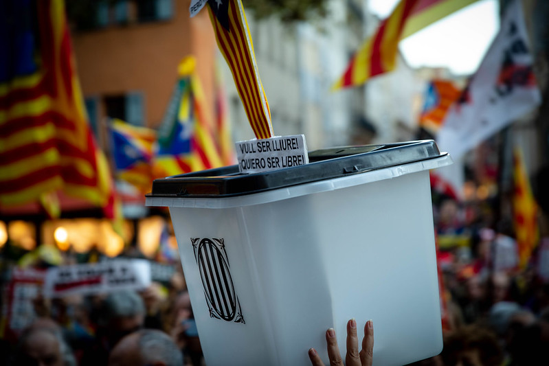 Urna de votació blanca amb el lema «Vull ser lliure! Quiero ser libre» alçada sobre la multitud