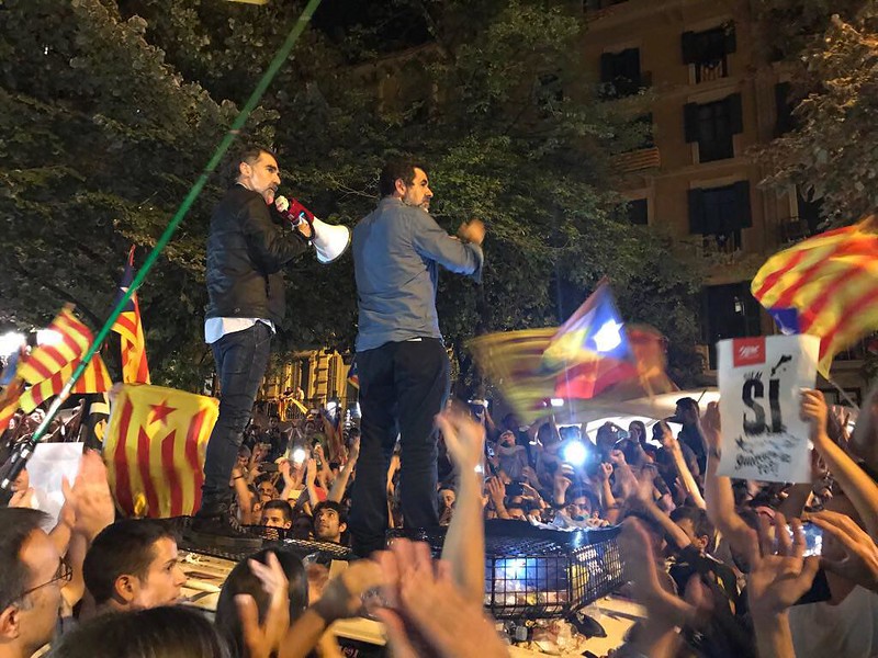 Dos homes parlen amb un megàfon des d’un vehicle, entre una multitud amb esteledes, de nit
